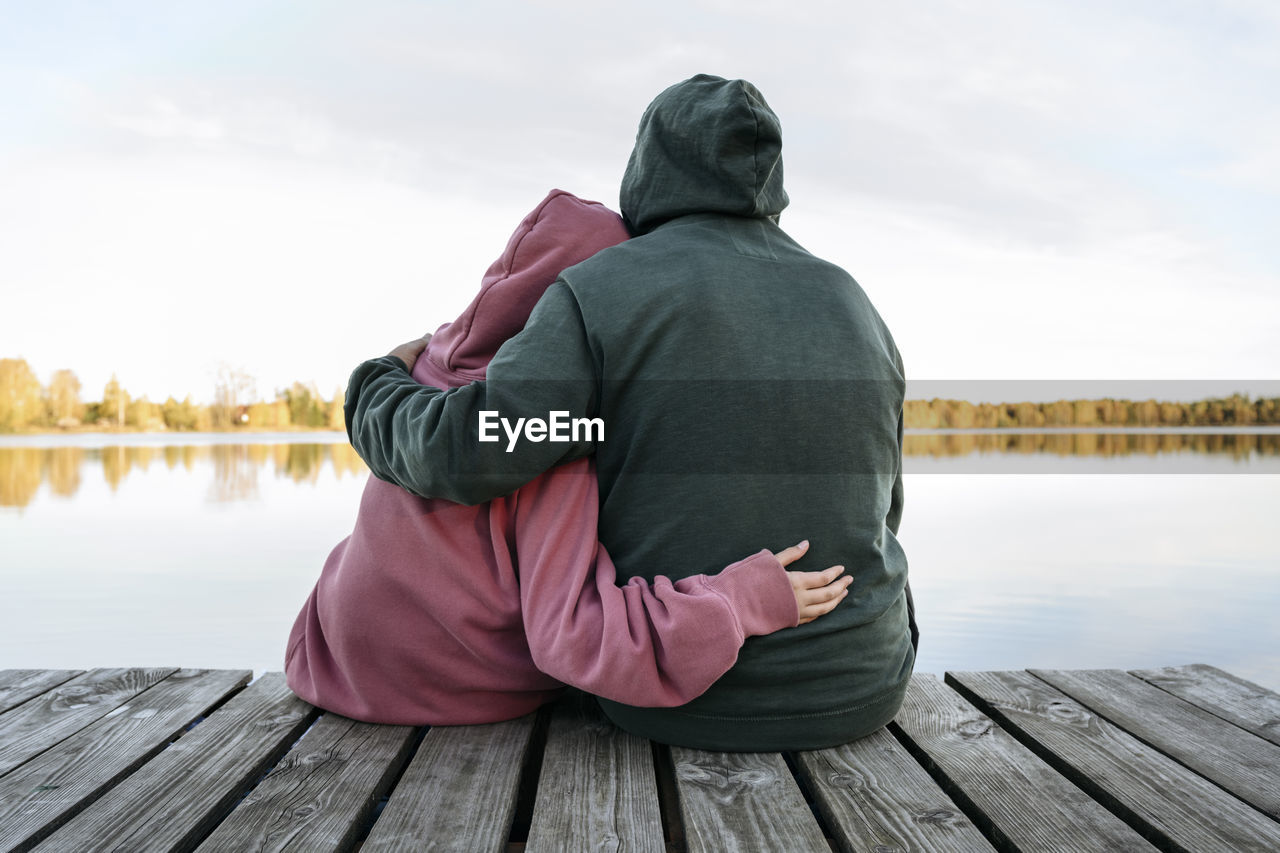 Senior man embracing granddaughter on jetty in front of lake