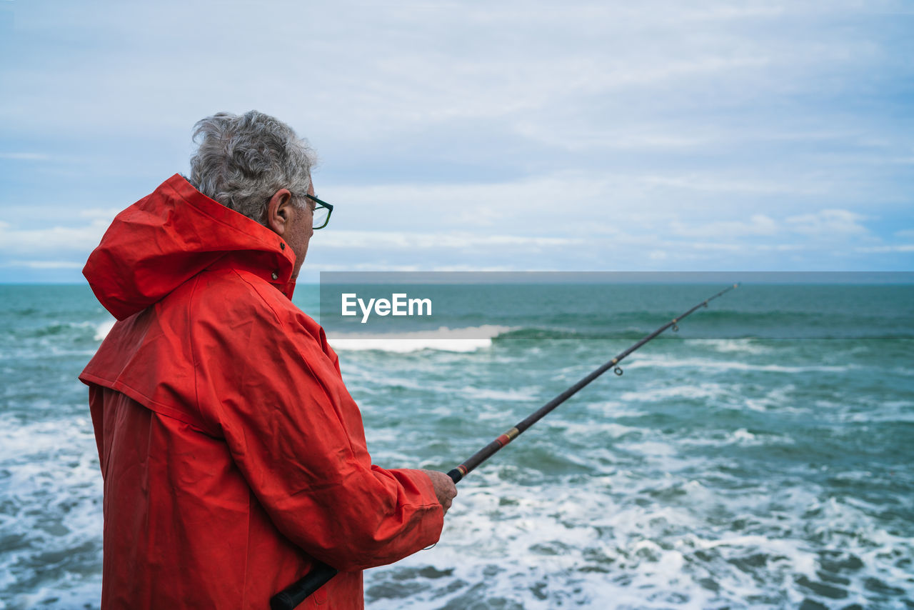 MAN WITH RED UMBRELLA STANDING IN SEA AGAINST SKY