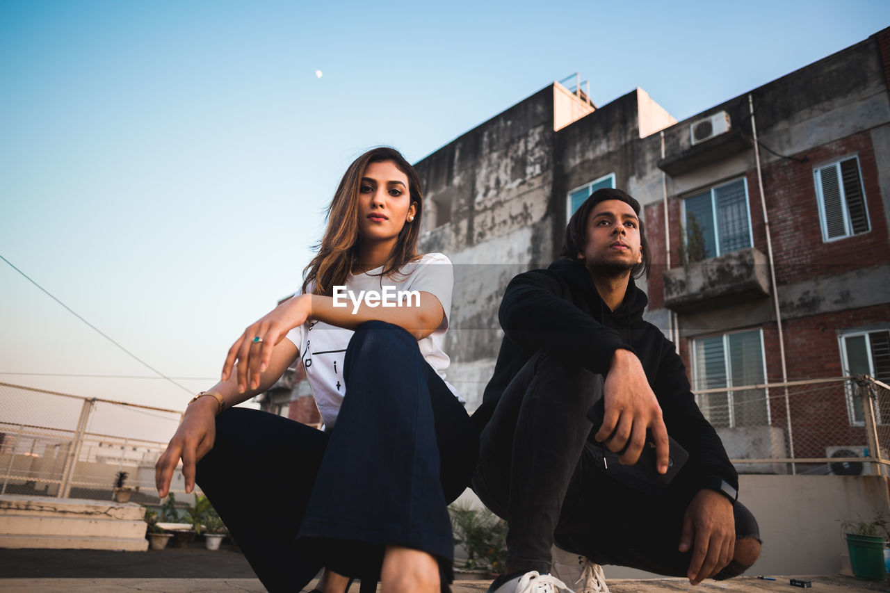 YOUNG WOMAN SITTING ON CITY AGAINST SKY