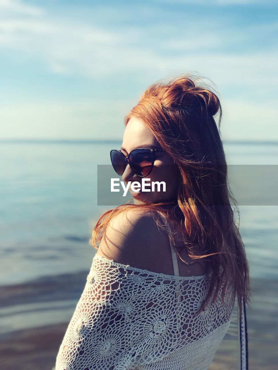 Young woman wearing sunglasses at beach against sky