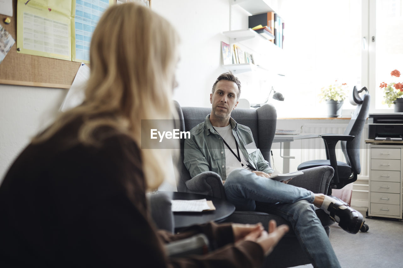 Full length of male counselor listening to female student discussing in school office