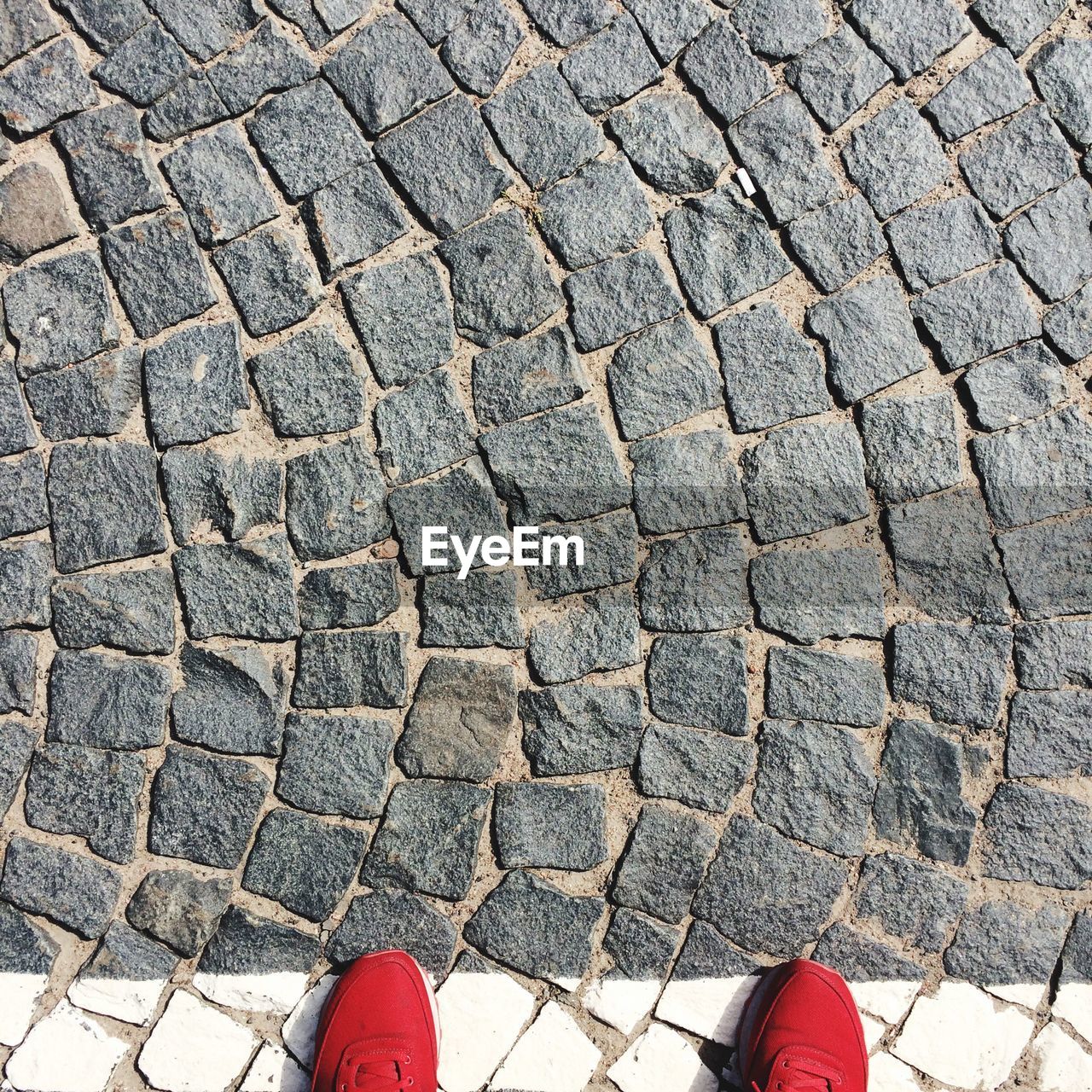 HIGH ANGLE VIEW OF PERSON STANDING ON COBBLESTONE