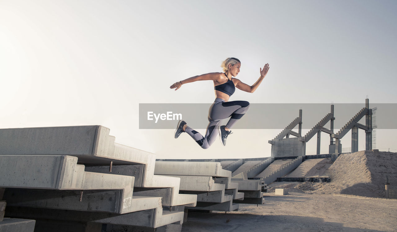 Female athlete jumping by built structure against sky