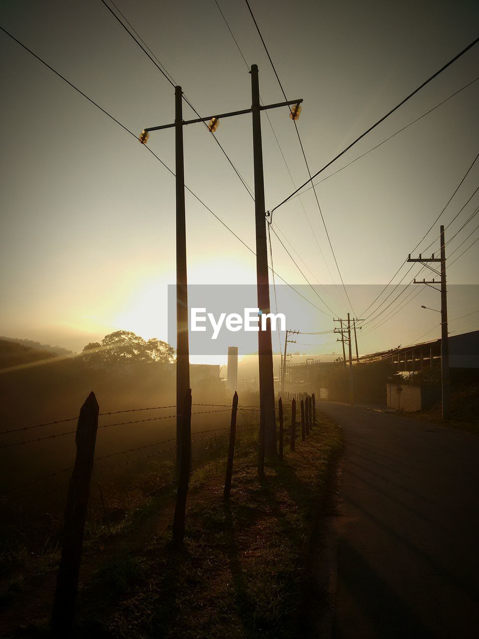 ELECTRICITY PYLON ON LANDSCAPE AGAINST SKY AT SUNSET