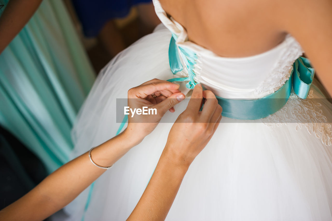 Close-up of woman assisting bride for getting dressed