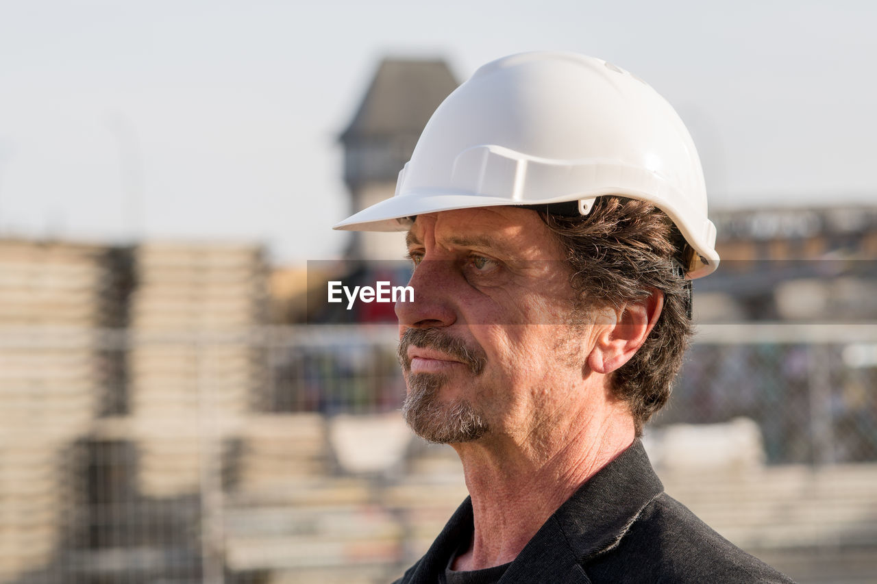 Close-up of thoughtful architect standing against buildings