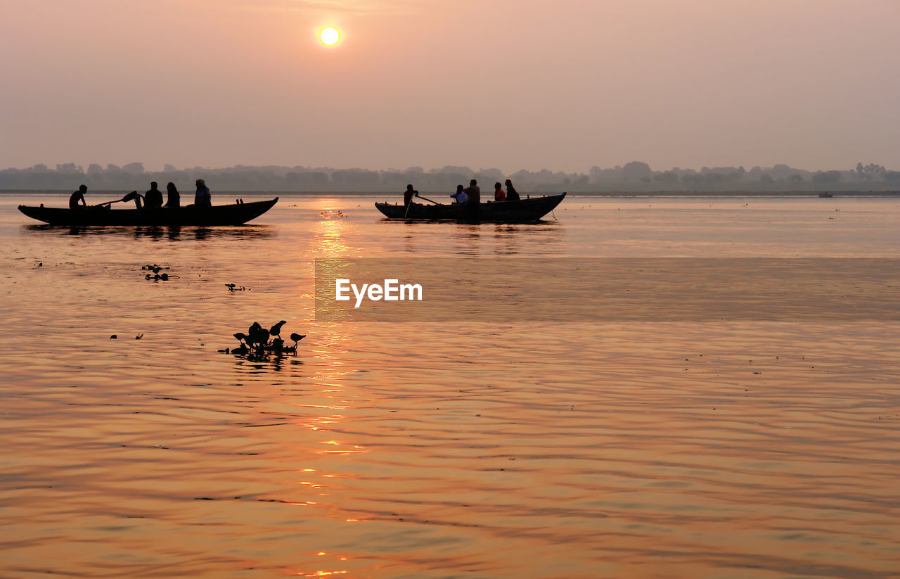 SILHOUETTE PEOPLE ON BOAT IN SEA AGAINST SKY DURING SUNSET