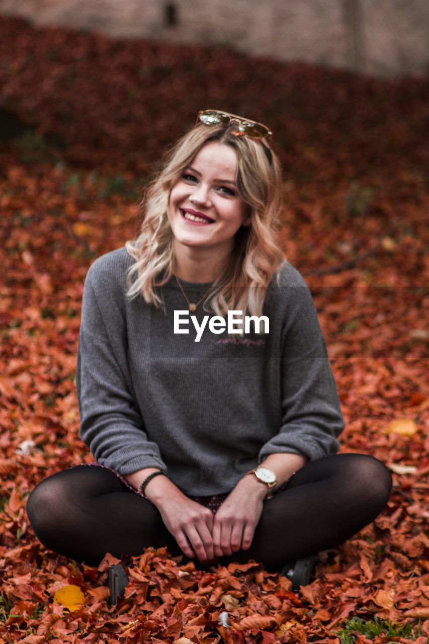 Portrait of smiling young woman sitting on autumn leaves