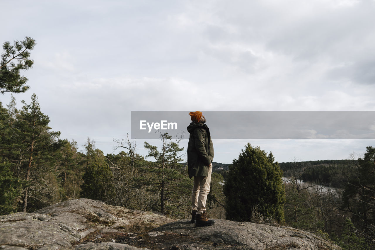 Mature man with hand in pocket standing on mountain against sky