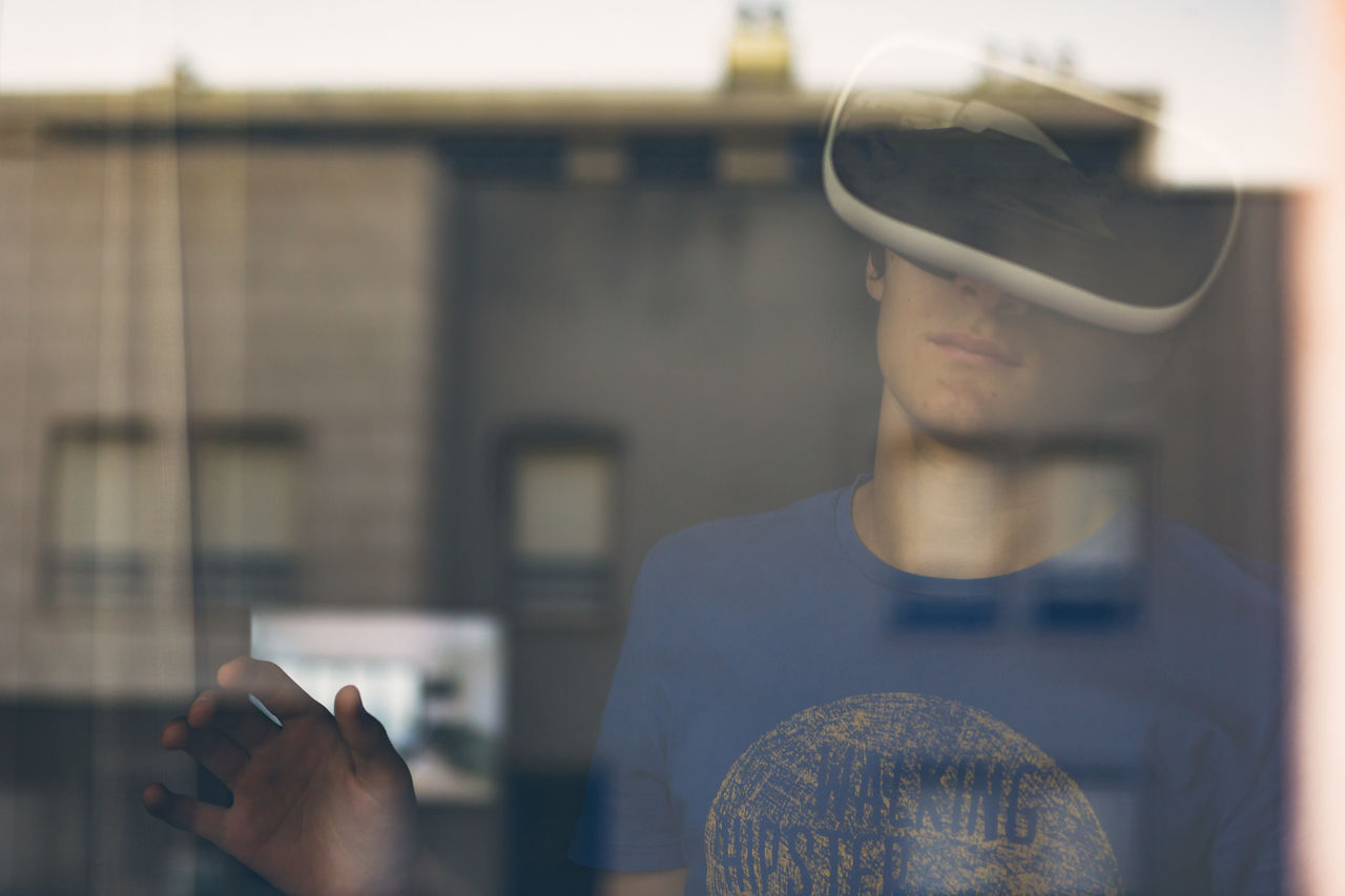 Teenage boy wearing virtual reality simulator seen through window