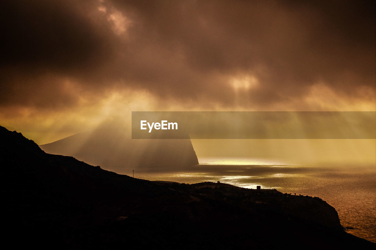 Silhouette mountain by sea against sky at night