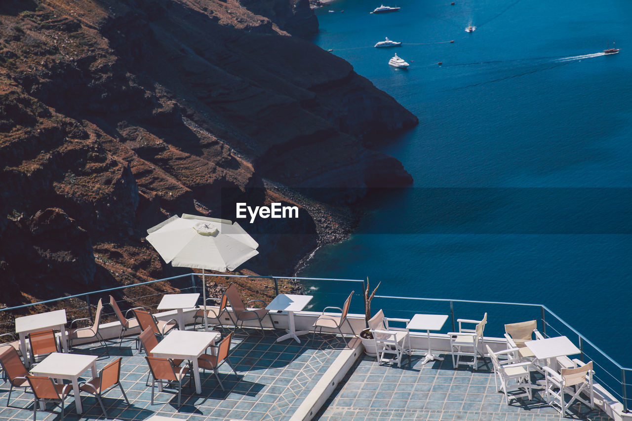 High angle view of chairs and tables with umbrella on building terrace by sea