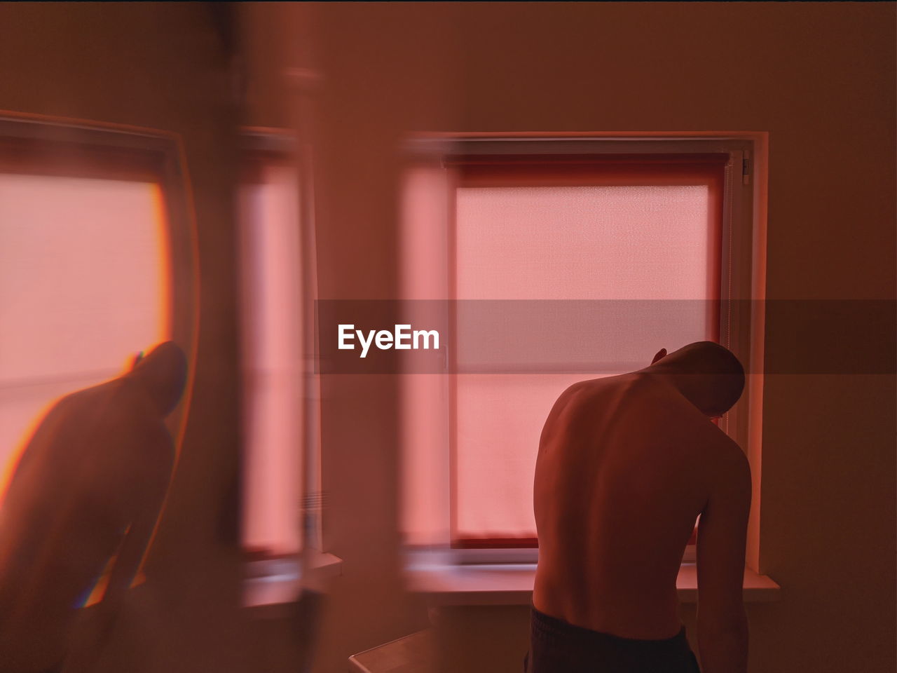 Rear view of shirtless man standing by window at home