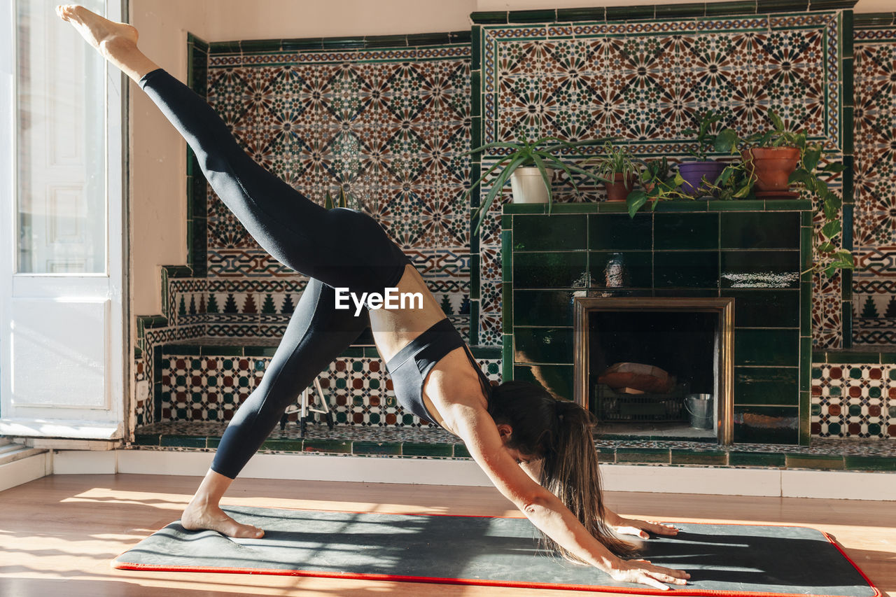 Fit woman practicing eka pada adho mukha svanasana at home