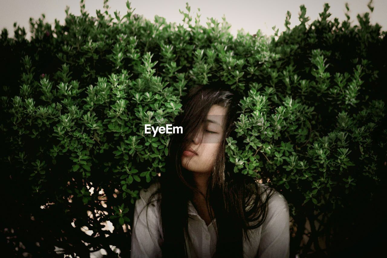 Young woman with eyes closed sitting amidst plants