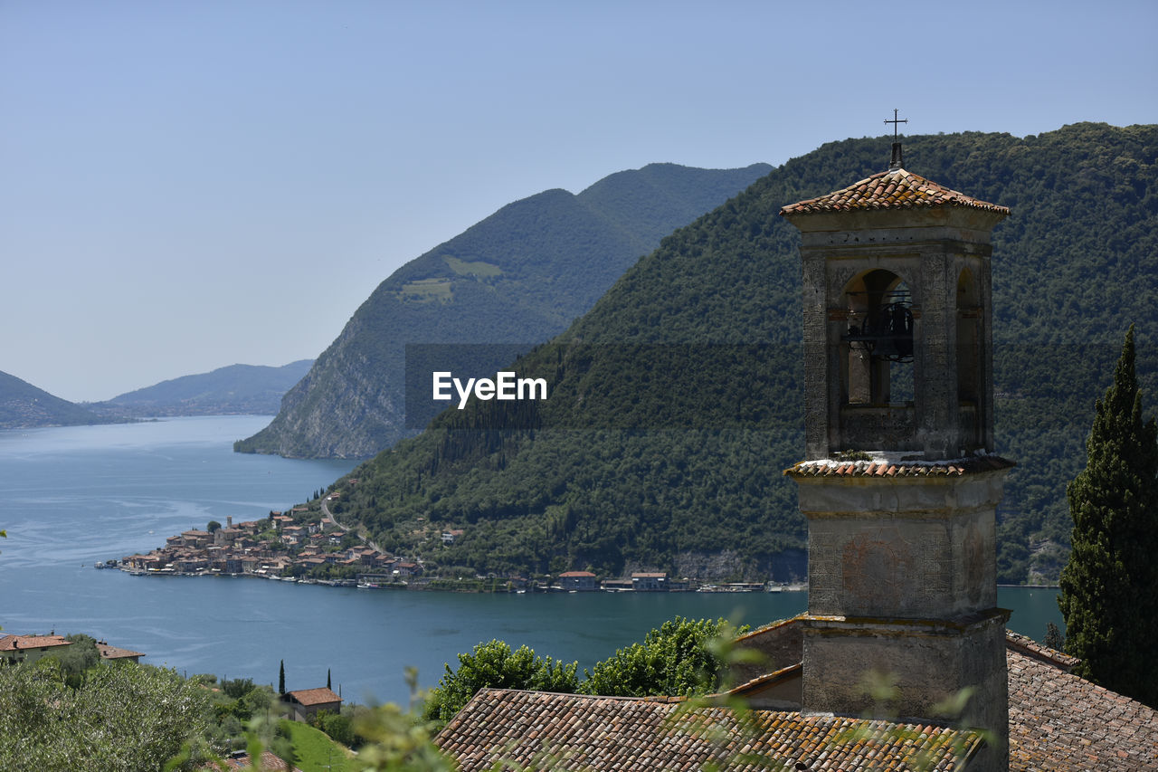 Italy, lombardy, lake iseo surrounded by forested mountains with bell tower in foreground