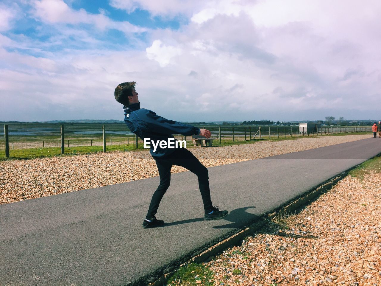 Full length of young man bending on road against cloudy sky during sunny day