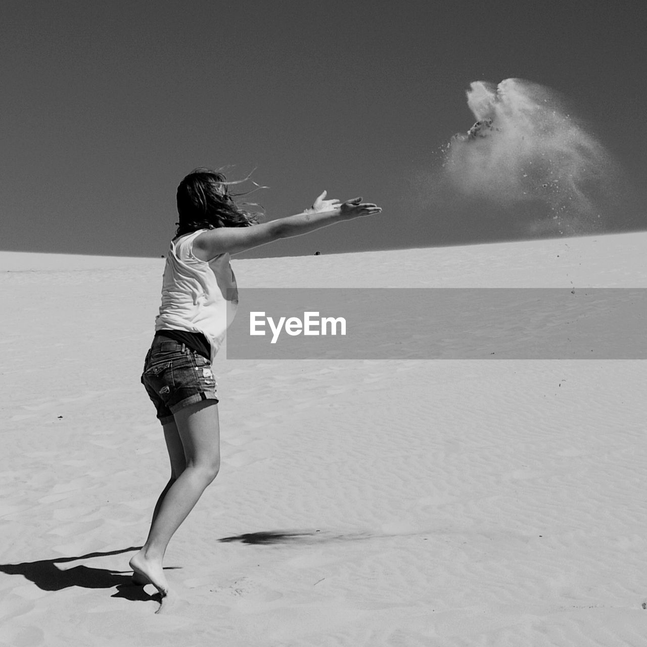 Woman throwing sand at beach against sky