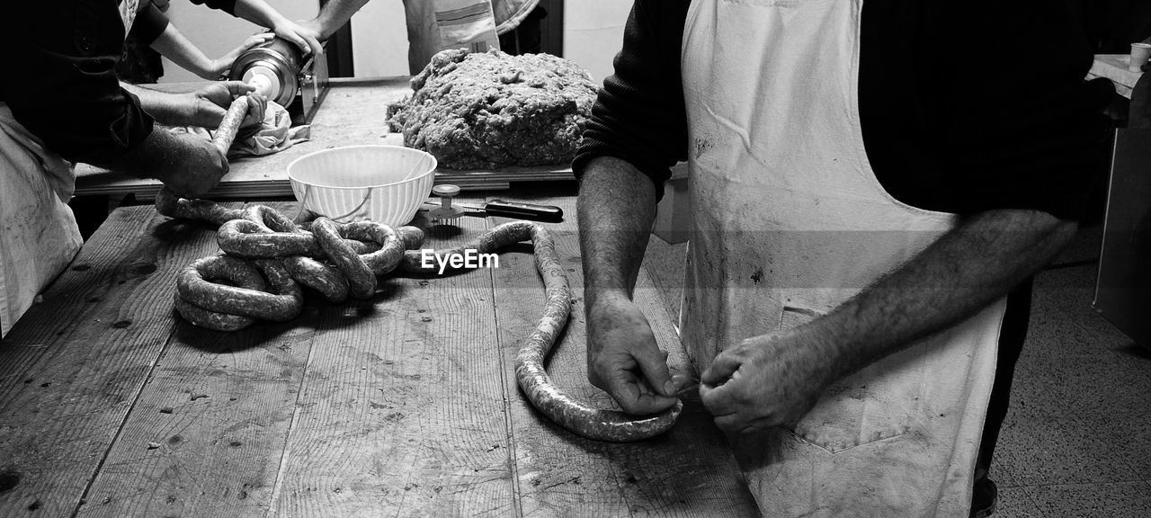 Midsection of men making pork sausage roll