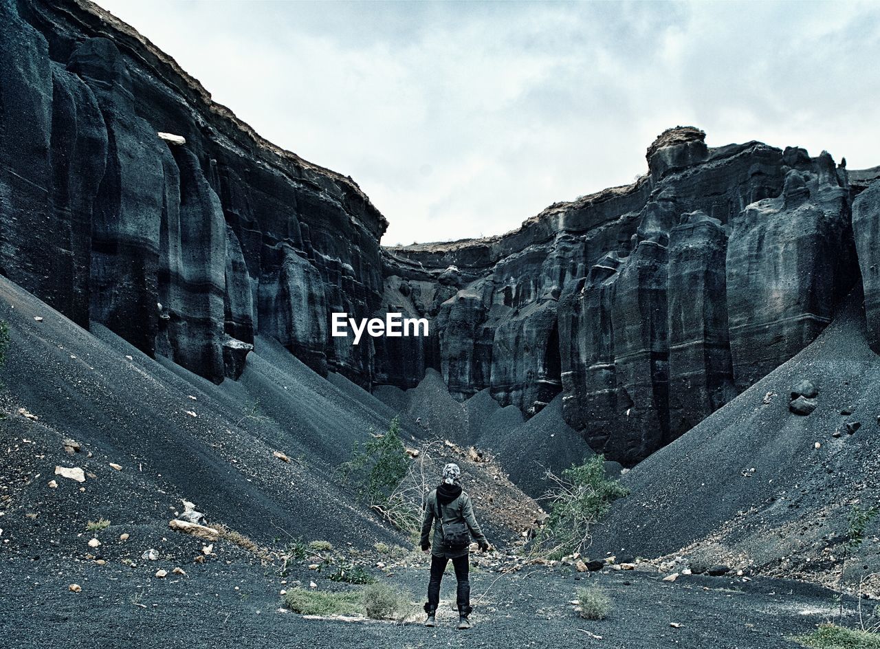 Rear view of person looking at rocky mountains against sky