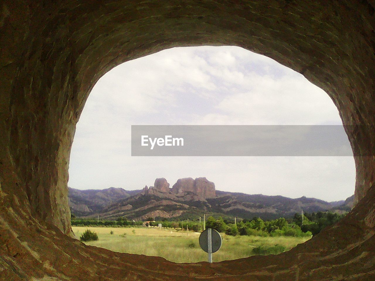 View of field against sky seen through cave