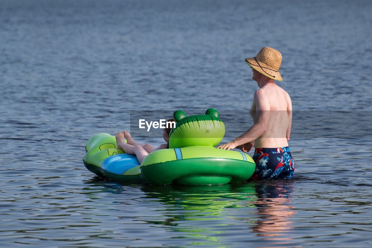 Shirtless man with daughter on inflatable raft in lake