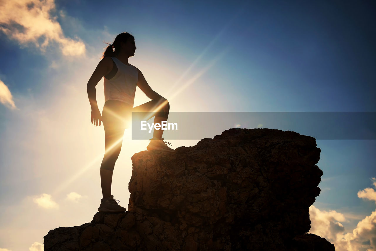Low angle view of woman standing on rock formation against sky