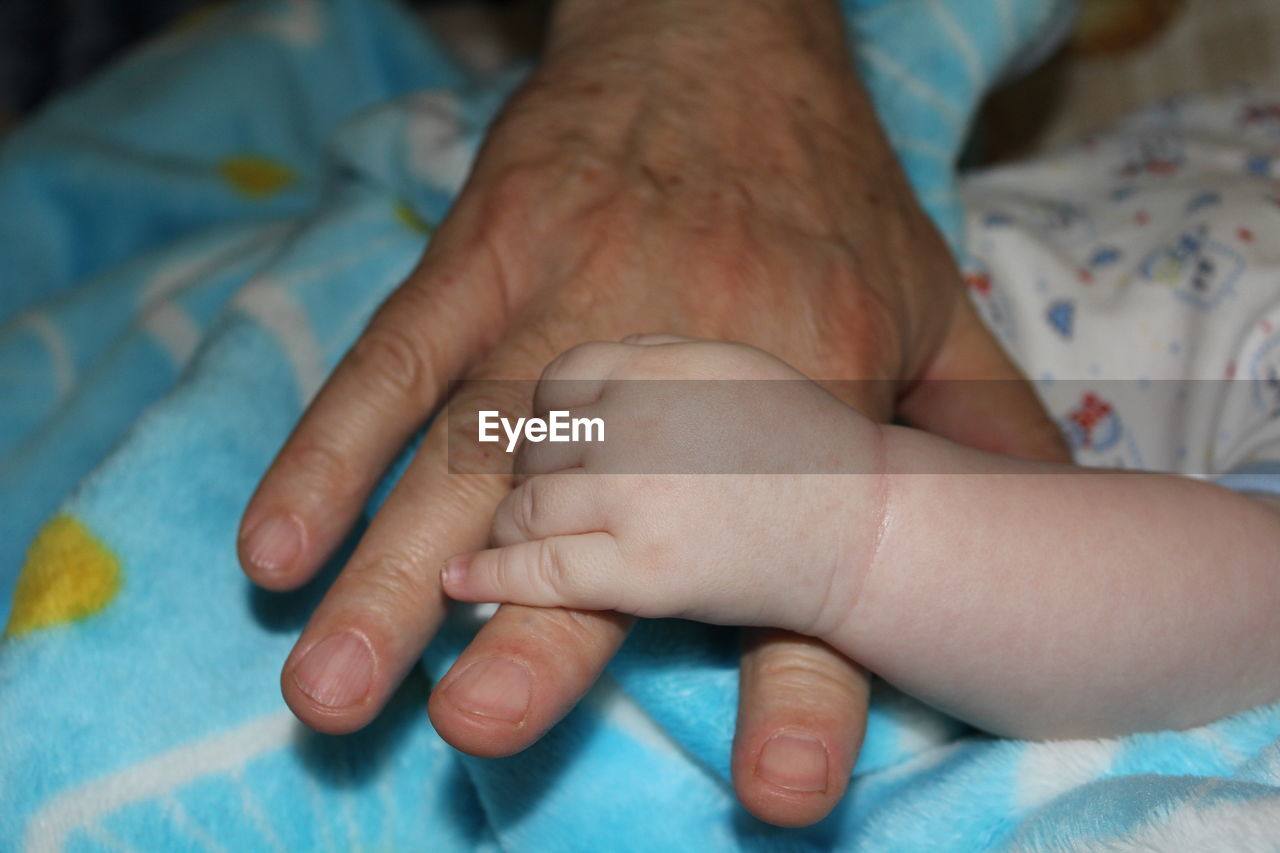 Cropped image of parent and baby holding hands at home