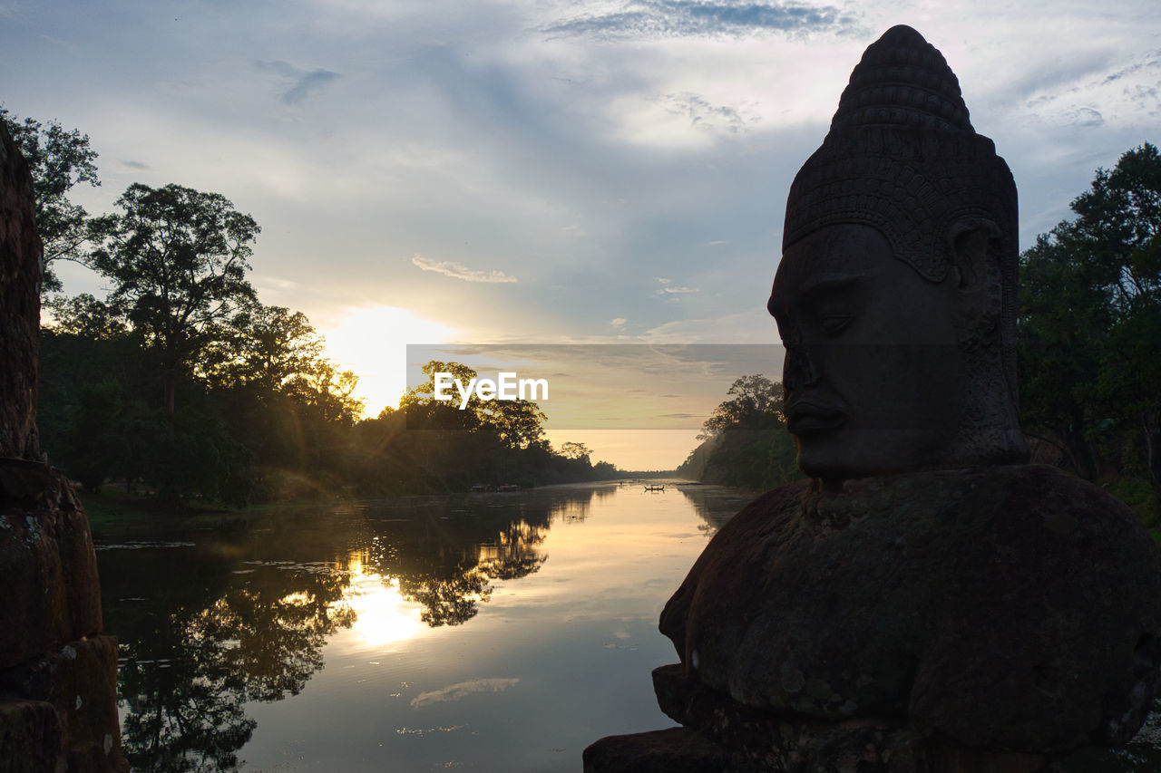 Low angle view of asian statue against sky during sunset with water