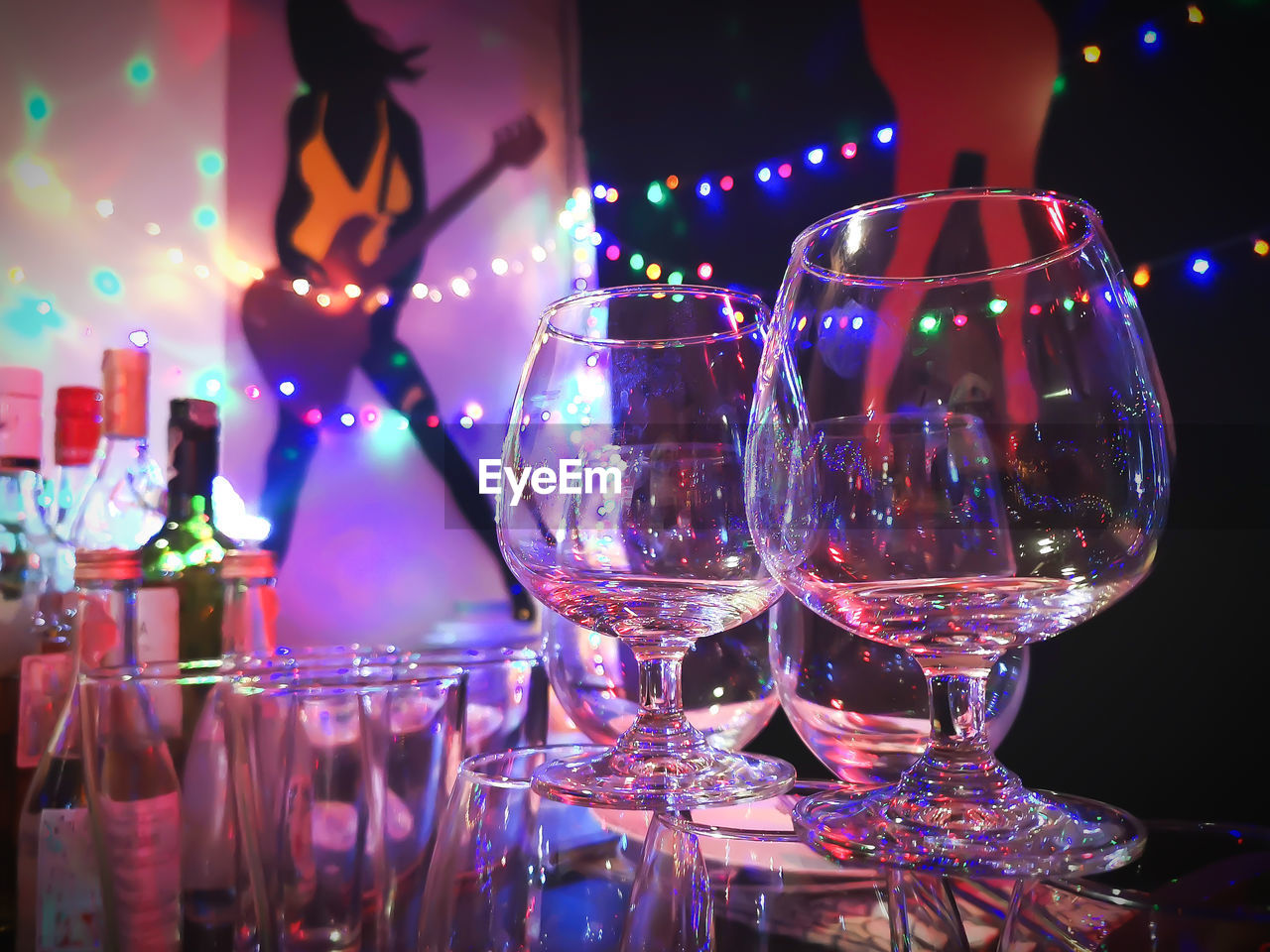 CLOSE-UP OF WINE GLASS ON TABLE AGAINST ILLUMINATED LIGHTS