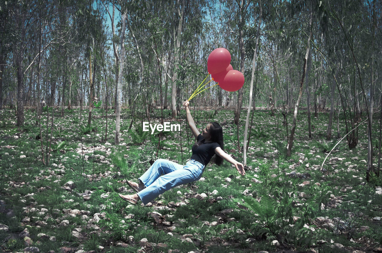 REAR VIEW OF WOMAN WITH HEART SHAPE BALLOON IN FOREST