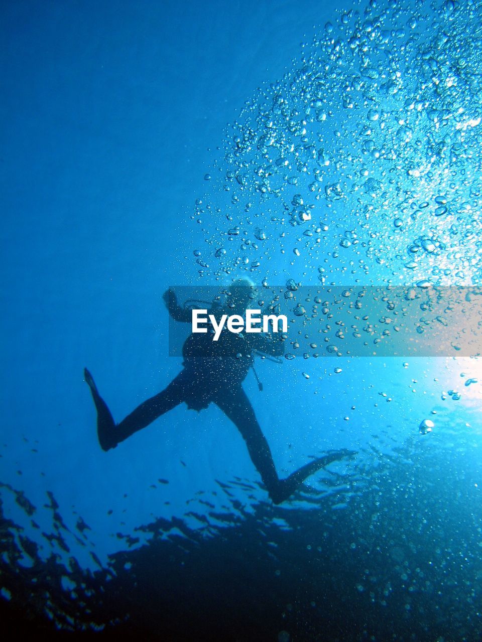 Low angle view of silhouette scuba diver swimming in blue sea