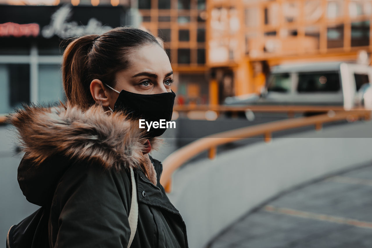 Young woman wearing mask looking away while standing in city