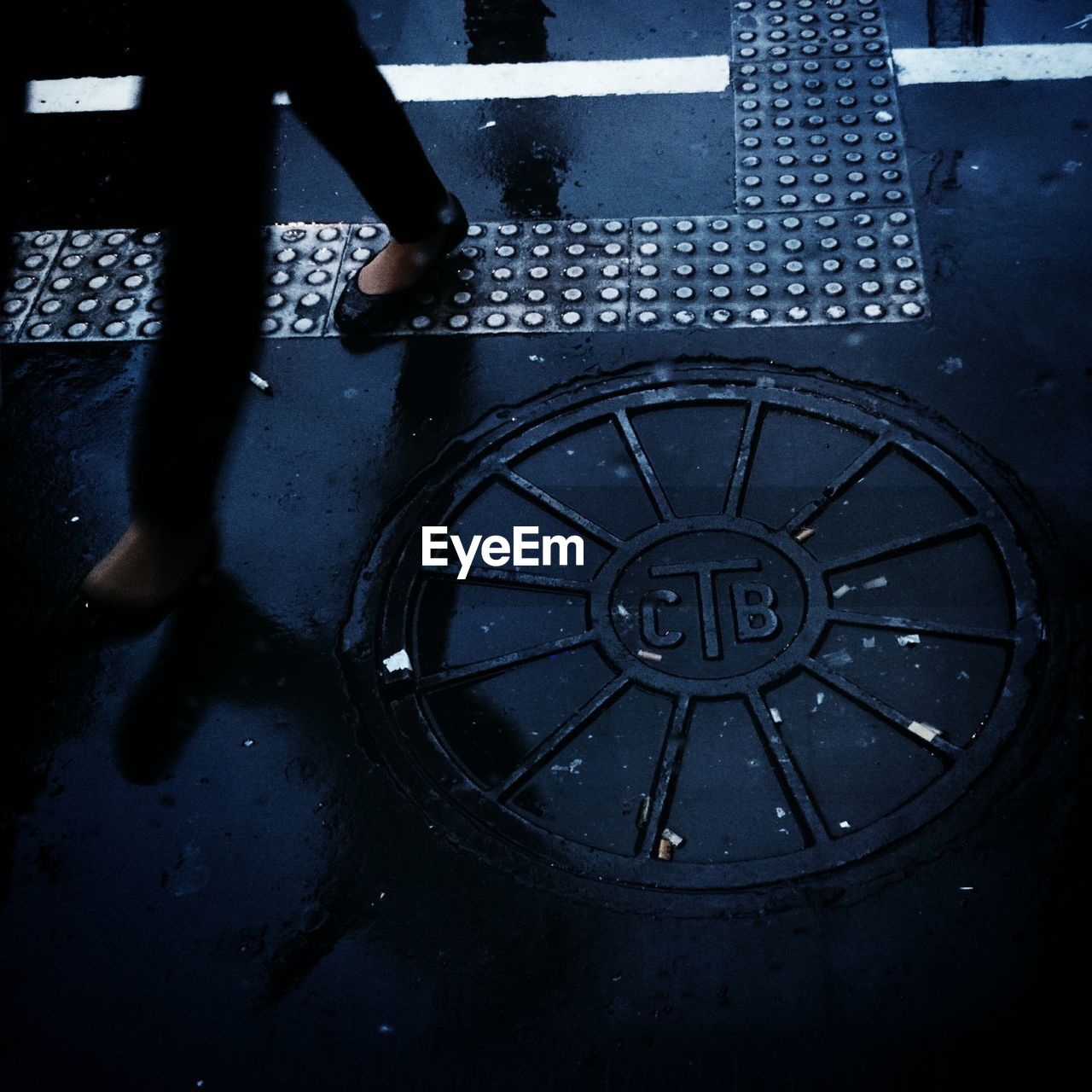 Low section of woman walking by manhole on city street