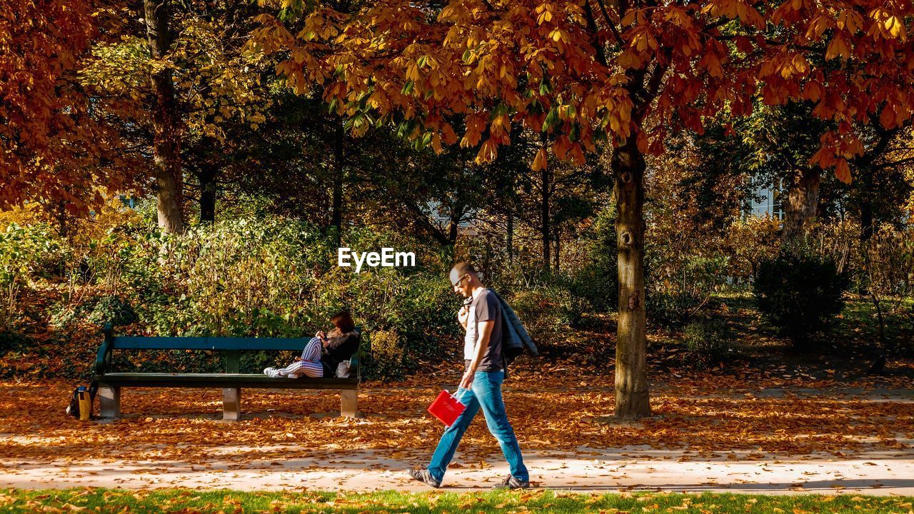 WOMAN SITTING ON BENCH AT PARK DURING AUTUMN