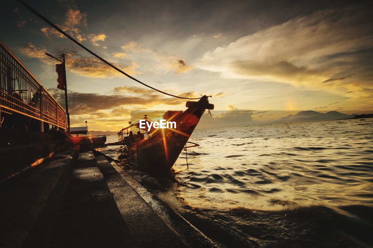 Boat moored on beach against sky during sunset