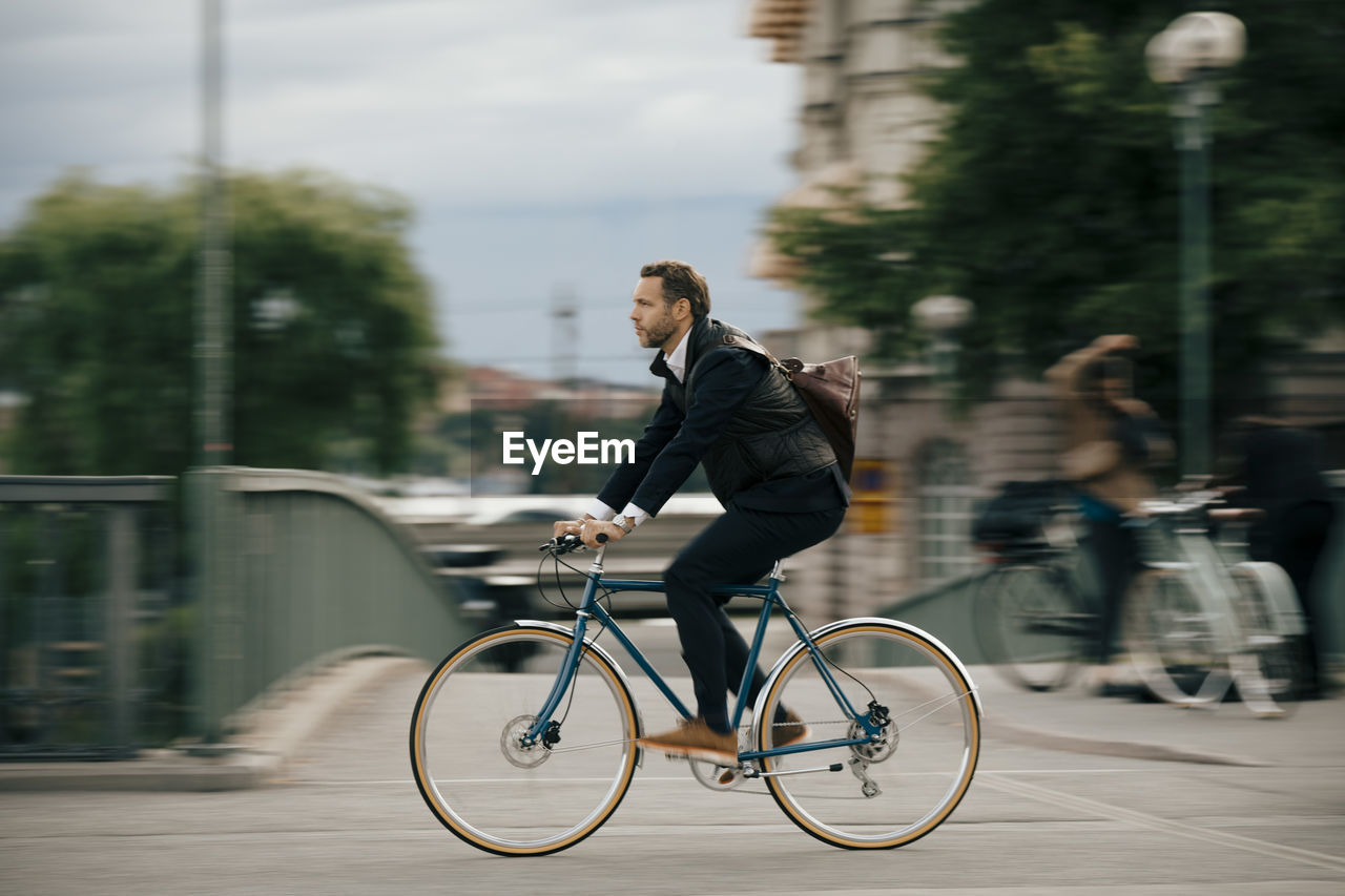 Full length of confident businessman cycling on bridge