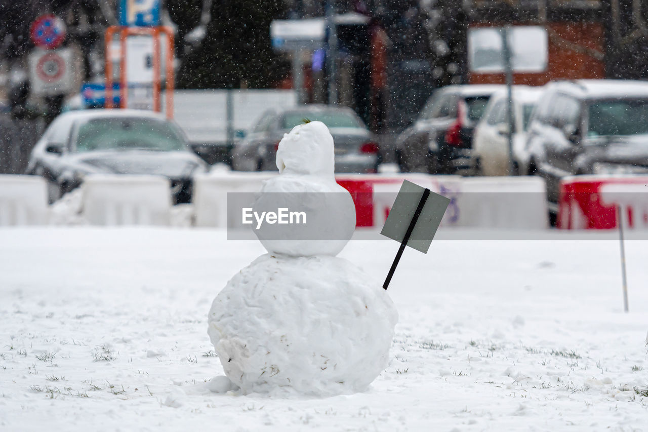 Snowman in the yard of a residential house, isolated on a defocused city background