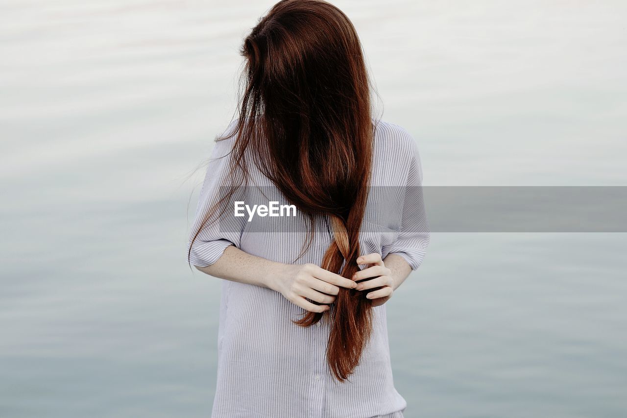 Young woman doing her hair against lake