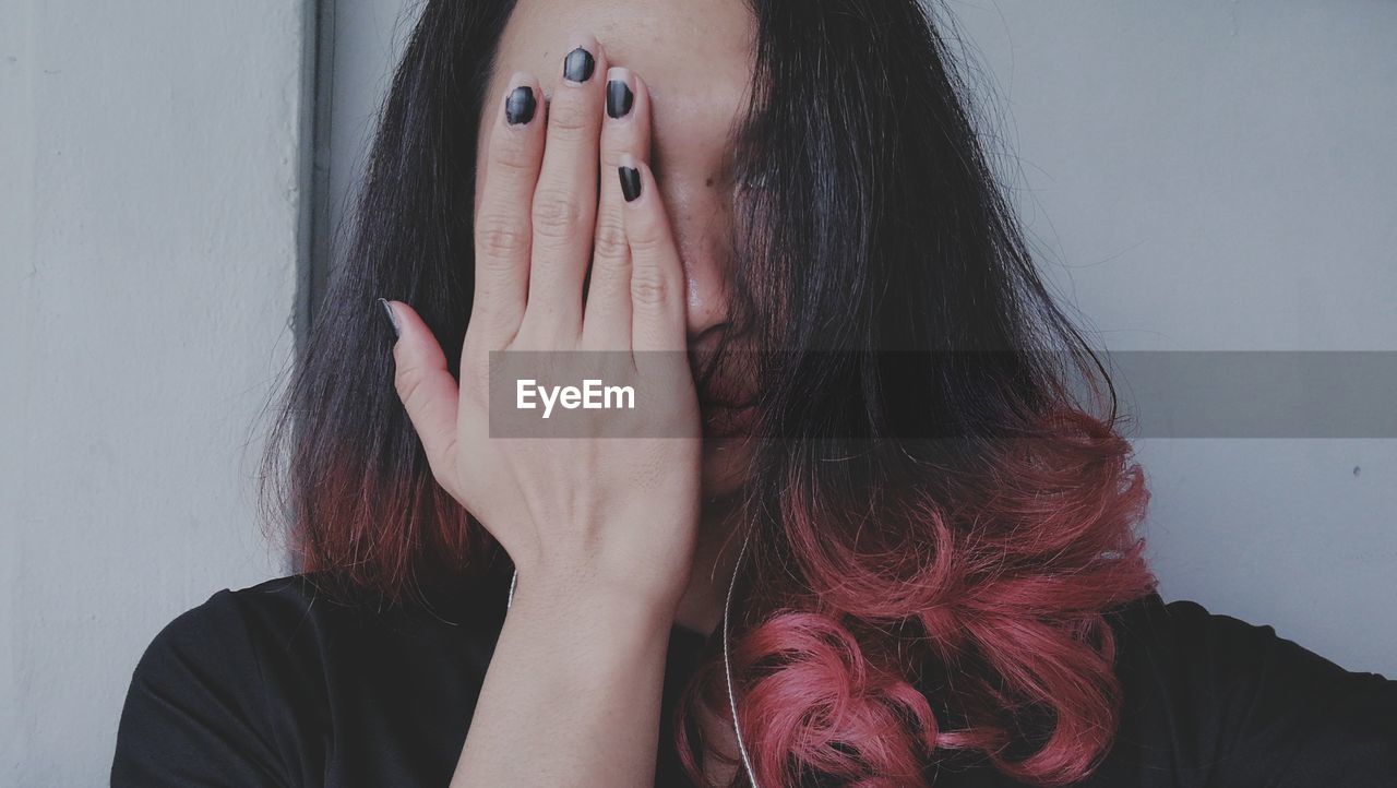 Woman covering face with eyes against wall