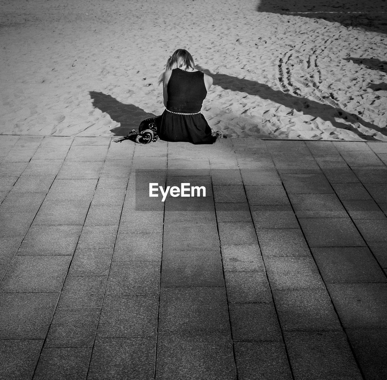 Rear view of woman in black dress sitting at beach