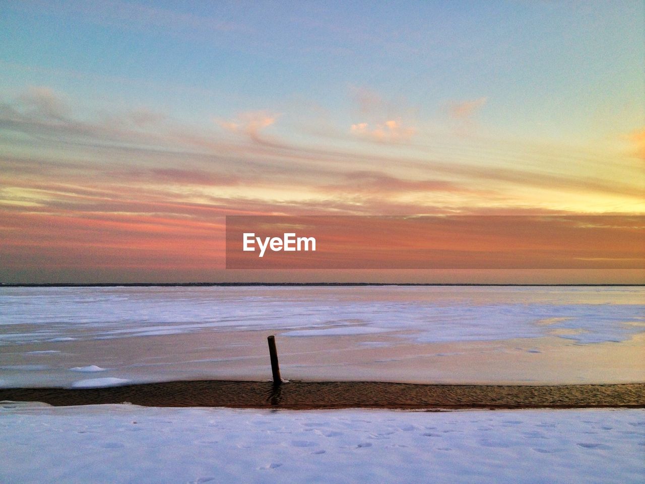 Frozen river against sky during sunset