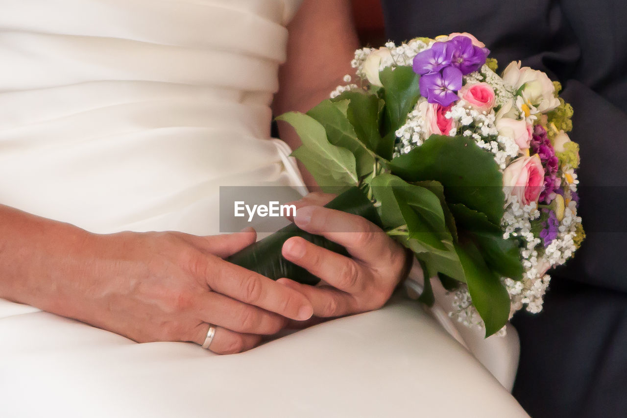 Midsection of bride and groom holding bouquet