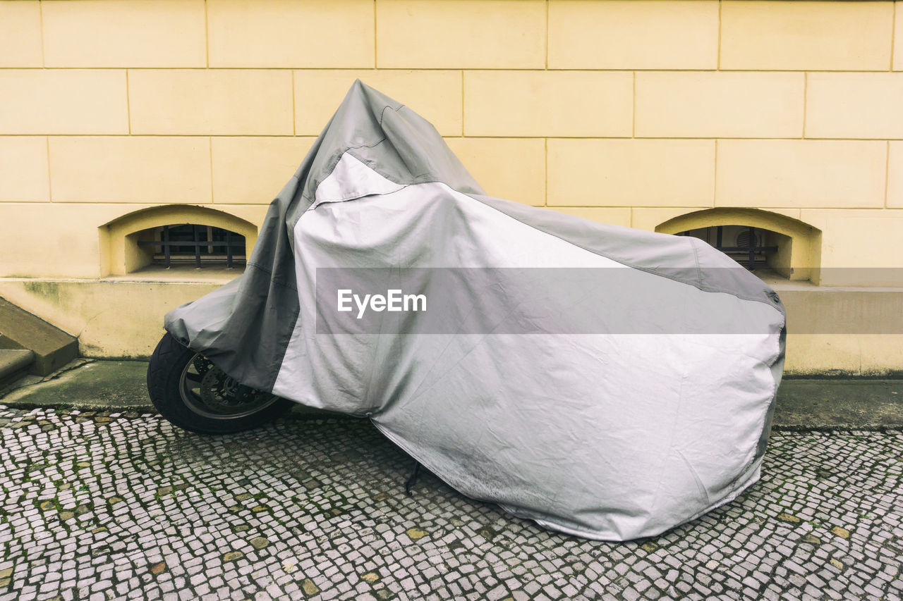 Motorcycle covered with fabric parked against wall