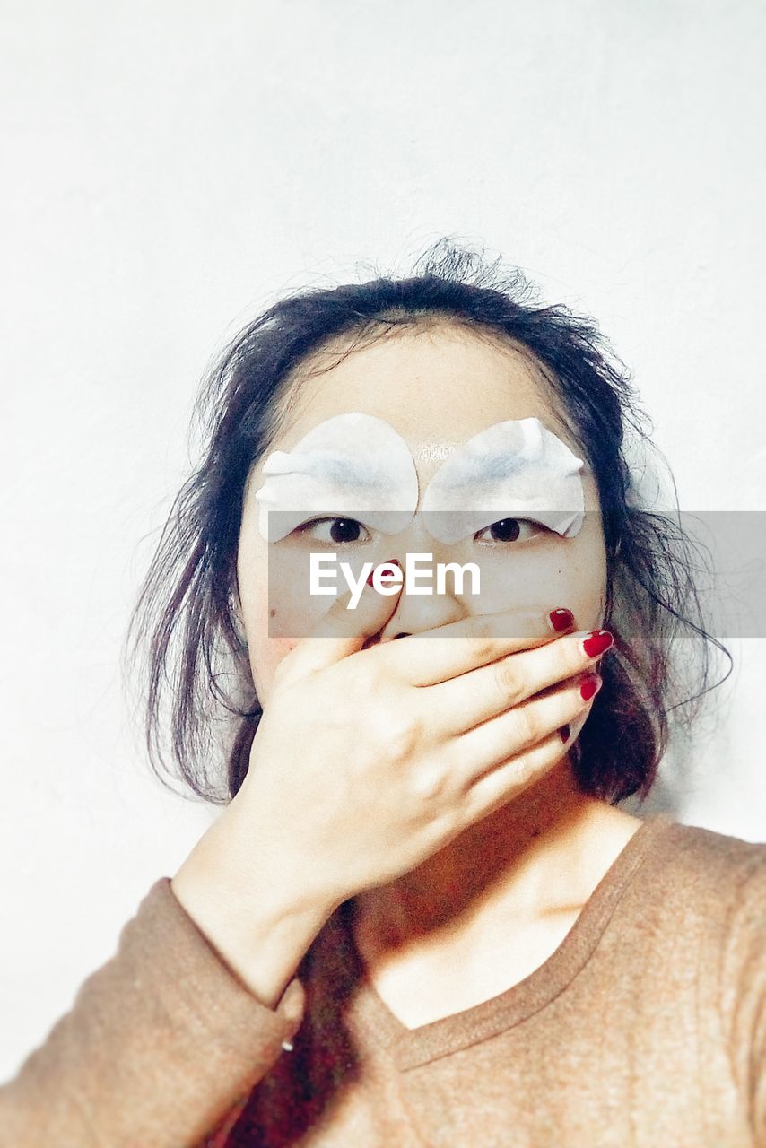 Close-up of woman with hand covering mouth against white background