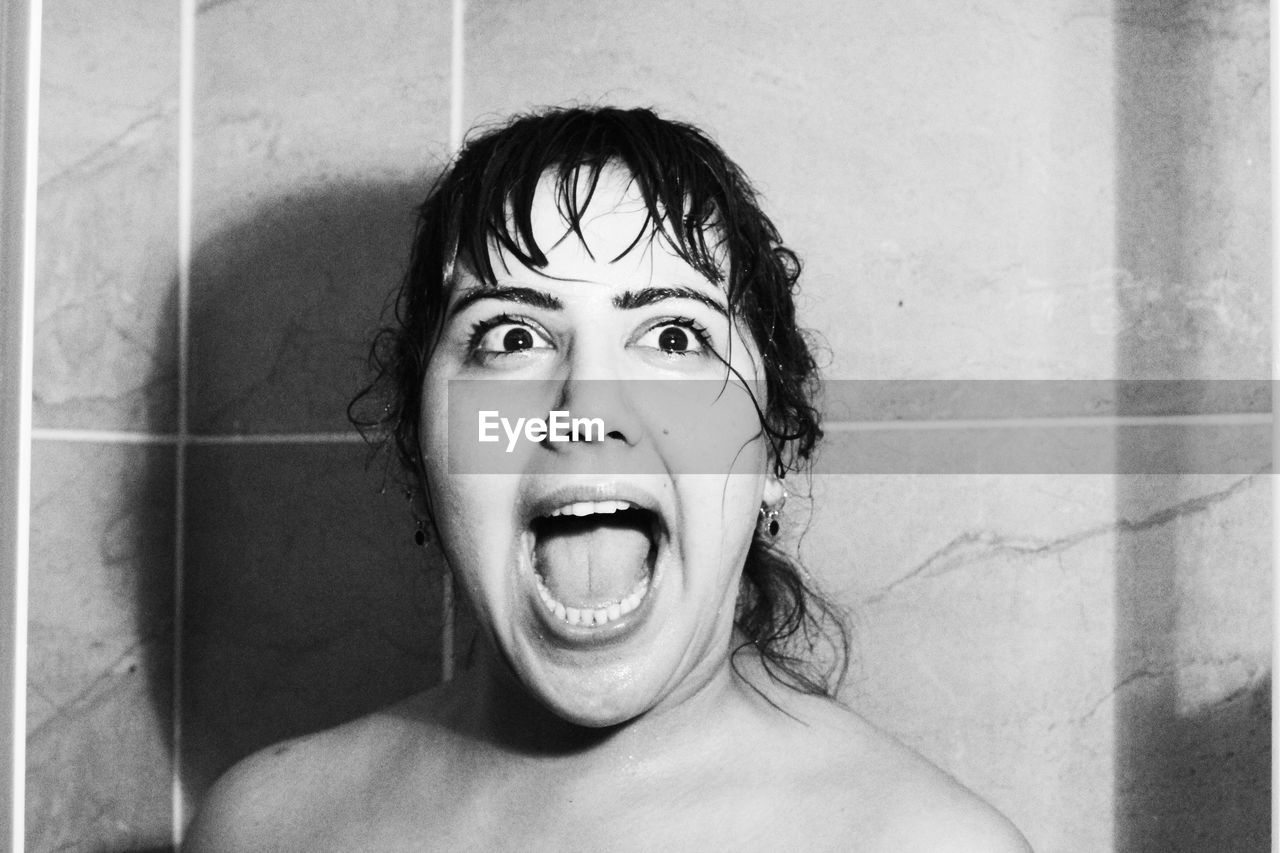 Shirtless young woman screaming against wall in bathroom