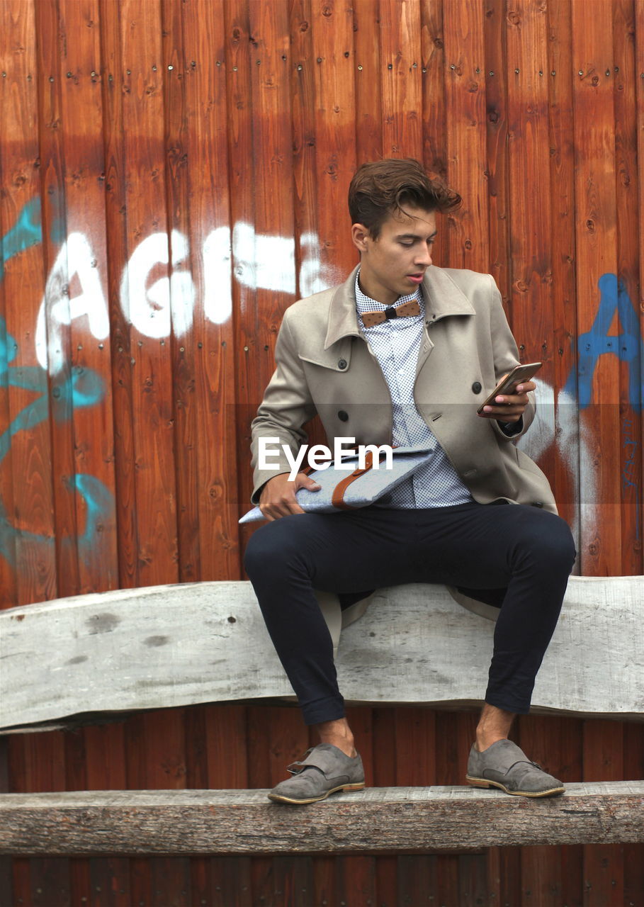 Young model using mobile phone while sitting on bench