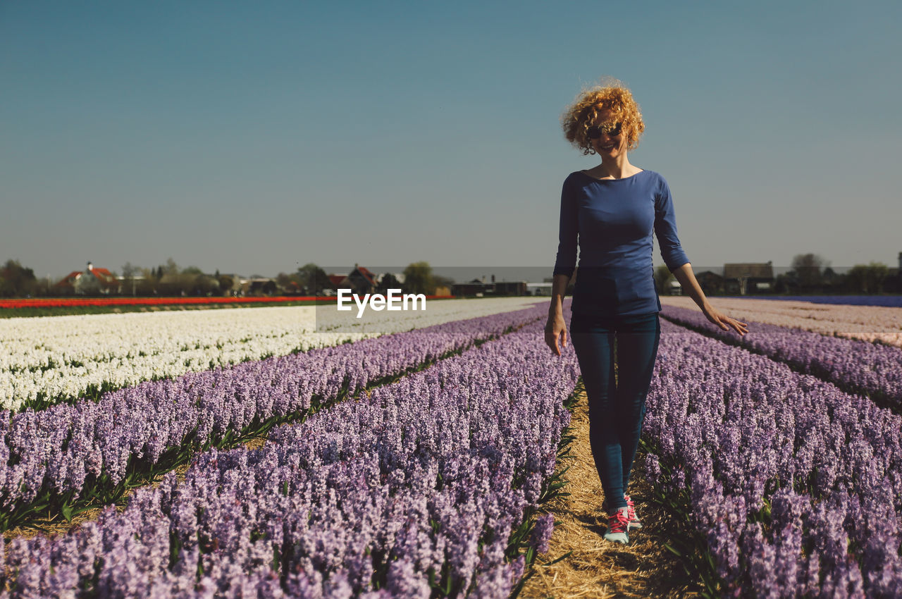 Woman walking in flower field against clear sky