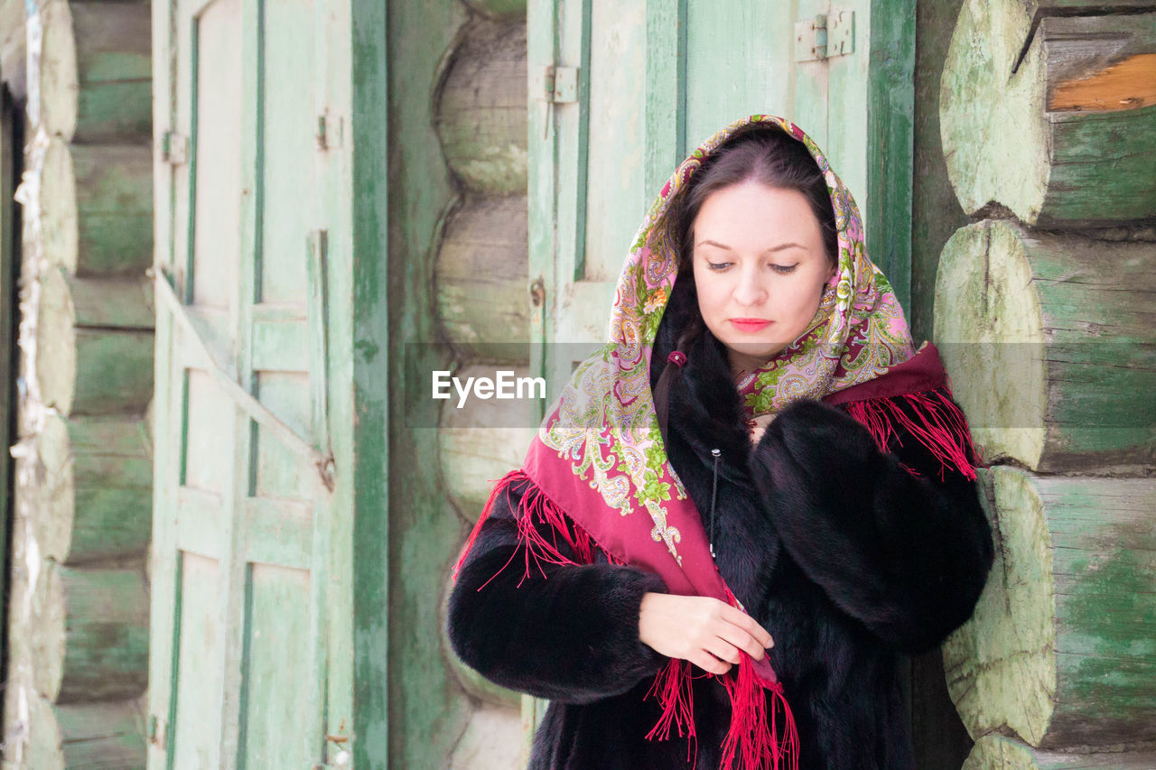 Woman wearing scarf looking away against log cabin