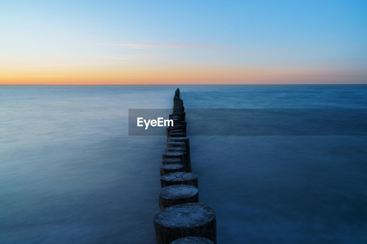 Wooden posts in sea against sky during sunset